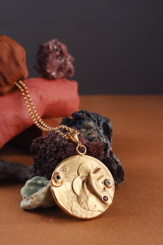 Product photo of Bocavolcan's beautiful Gold Plated 925 Silver Lahar necklace with Sapphire Ruby and Blue Sky Topaz stones handcrafted in Valencia, Spain with a background of volcanic rocks